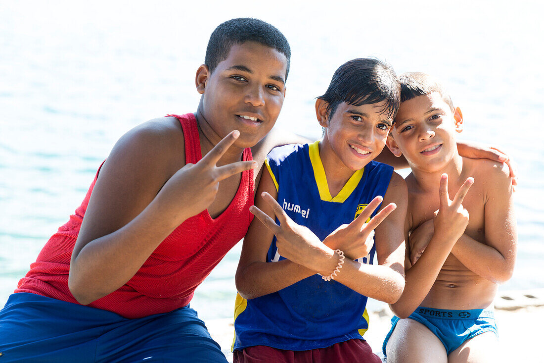 Three young local boys along the shore, victory sign, Cienfuegos, Cuba, Caribbean island