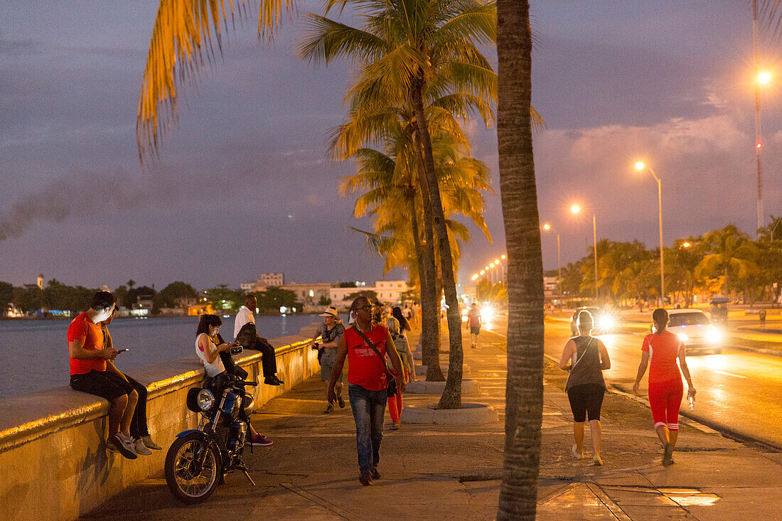 Oldtimer driving along the Malecon of Cienfuegos, meeting point in the evening and at night, nightlife, empty street, palm tree, colonial town, family travel to Cuba, parental leave, holiday, time-out, adventure, Cienfuegos, Cuba, Caribbean island