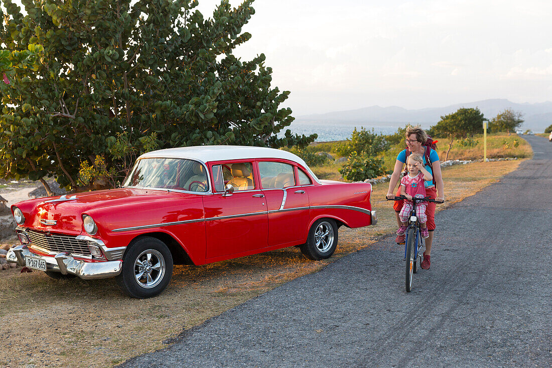 red oldtimer, woman with kid cycling along the lonely coast road from La Boca to Playa Ancon, with beautiful small beaches in between, turquoise blue sea, family travel to Cuba, parental leave, holiday, time-out, adventure, MR, La Boca, Trinidad, Cuba, Ca