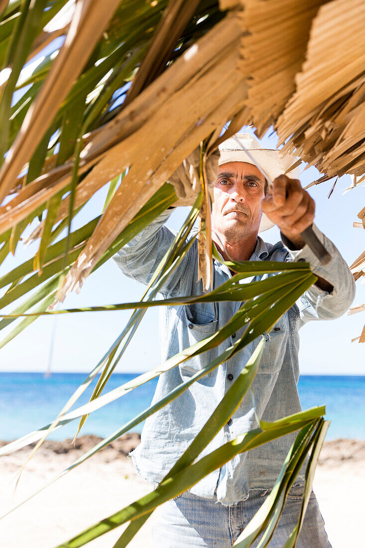 Kubaner, Mann repariert das Dach eines Sonnenschirmes aus Palmenblättern, einsame Küstenstraße von La Boca nach Playa Ancon, unterwegs gibt es viele schöne kleine Strände, Sandstrand, Einsamkeit, Naturverbundenheit, am Strand, türkisblaues Meer, schnorche