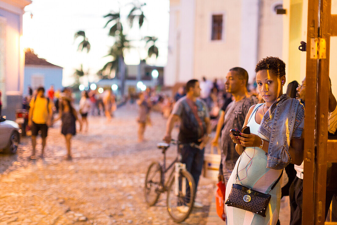 Kubanerin mit Handy, Frau, Schönheit, an den Terrassen von Trinidad an der Iglesia Parroquial de la Santisima Trinidad in der Nähe des Plaza Mayor, auf den Treppenstufen und im Café Trinidad Terraces treffen sich Touristen aus aller Welt, beliebter Platz,