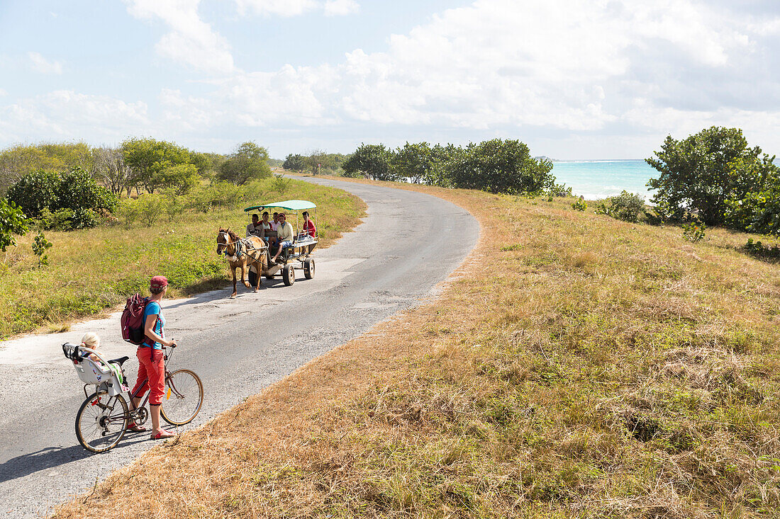 woman with child cycling along the lonely coast road from La Boca to Playa Ancon, with beautiful small beaches in between, turquoise blue sea, family travel to Cuba, parental leave, holiday, time-out, adventure, MR, near Trinidad, Cuba, Caribbean island