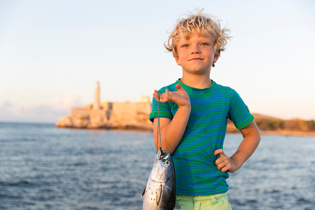 Junge, 6 Jahre mit einem Fisch am Malecon, Fischer, Tourist, Habana Vieja, Habana Centro, Altstadt, Zentrum, gegenüber Castillo De Los Tres Reyes Del Morro, Familienreise nach Kuba, MR, Havanna, Republik Kuba, karibische Insel, Karibik