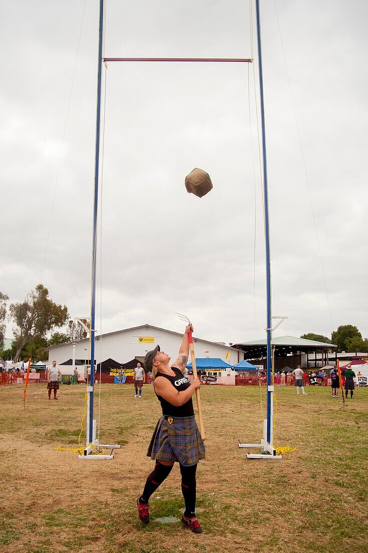 A kilted young woman competes in the 'Sheaf Toss' at a Scottish festival in Costa Mesa, CA, using a pitchfork to toss a 16-pound burlap bag of straw over a bar