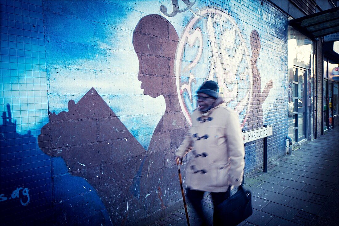 Old man with walking cane passing by graffiti on wall, East London, London, England