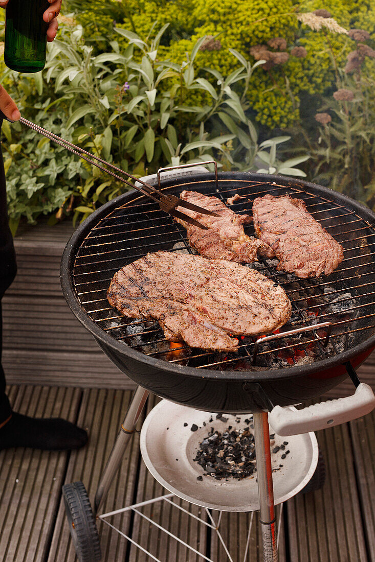 Cropped image of man cooking steak on barbecue grill on patio