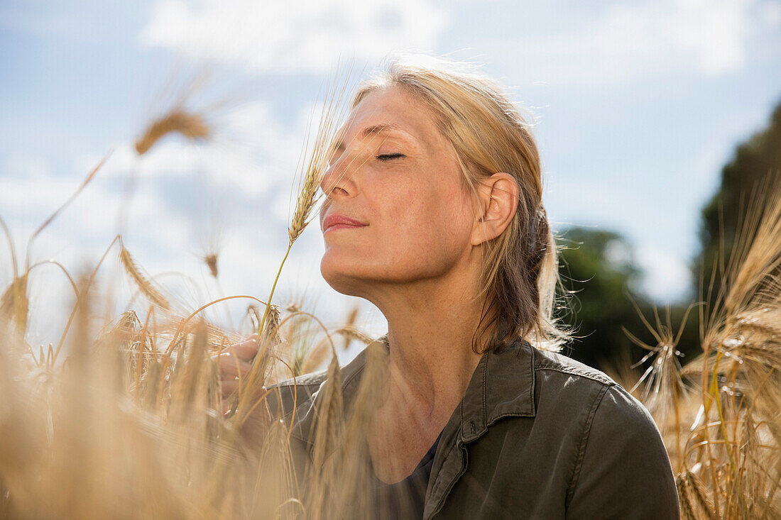 Thoughtful smiling woman with closed eyes resting amidst crops at farm on sunny day