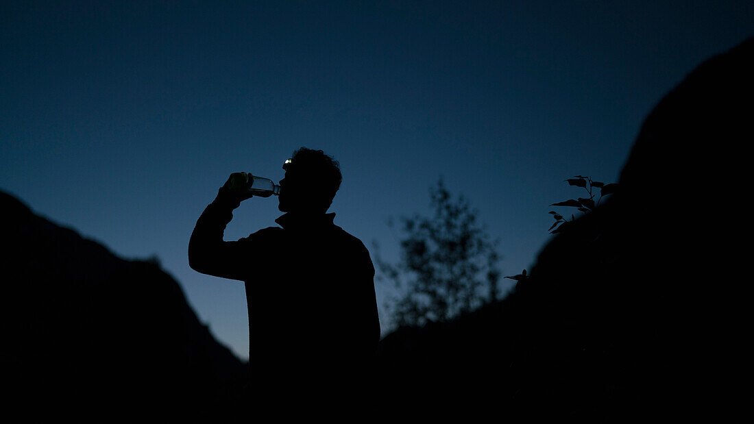 Silhouette man drinking water from bottle while standing on mountain at night