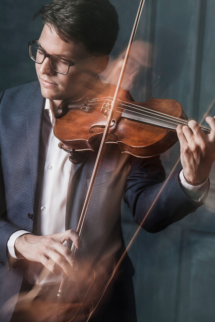 Blurred motion of handsome young man playing violin with closed eyes