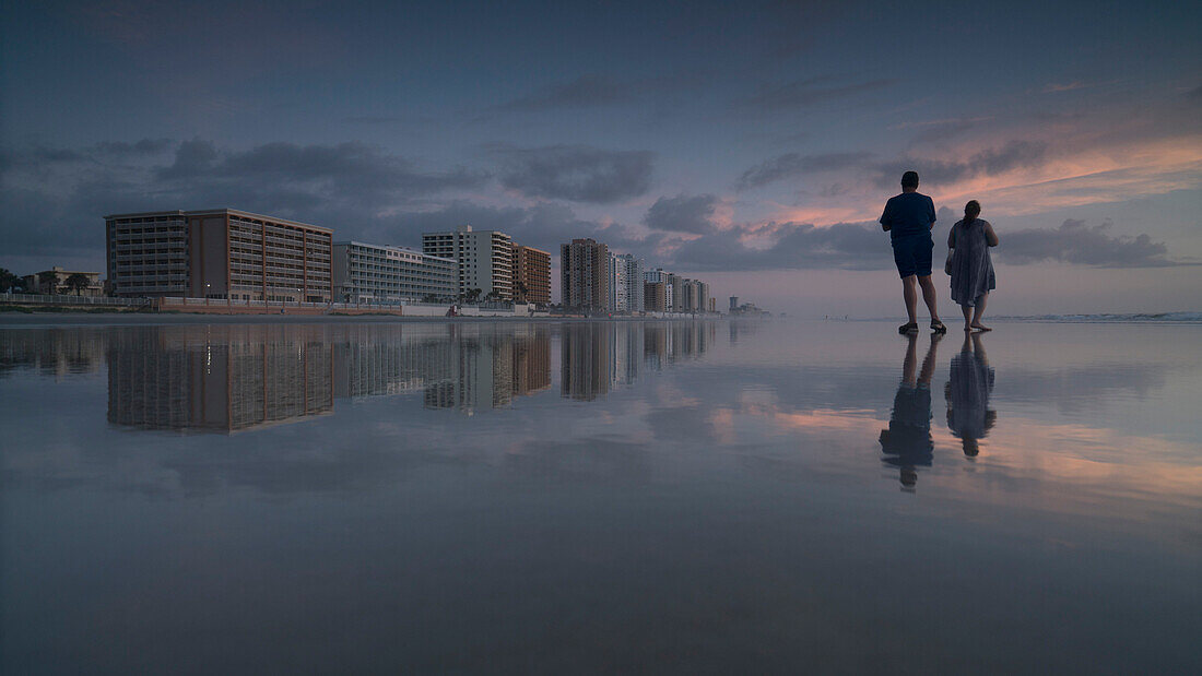 Young man and woman standing on shore at beach against sky during sunset, Daytona, Florida, USA