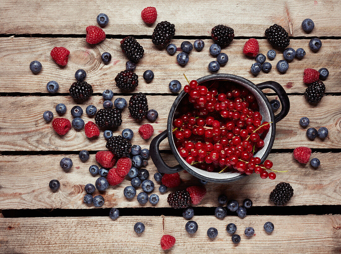 Directly above shot of red currants in container surrounded with berry fruits on table