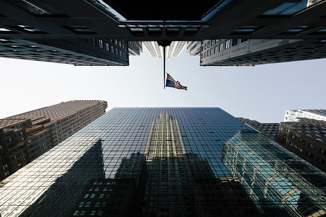 Directly below view of American Flag amidst modern office skyscrapers against sky, New York, USA