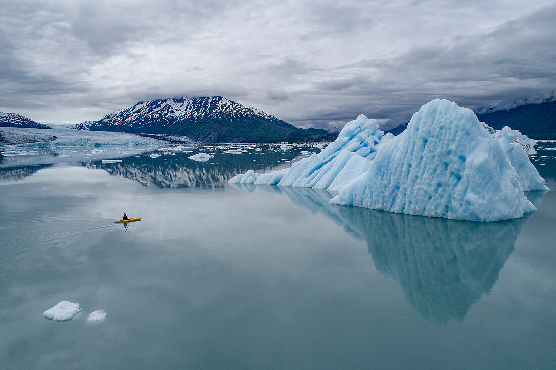 Person canoeing in lagoon by icebergs against cloudy sky, Lake George, Palmer, Alaska, USA