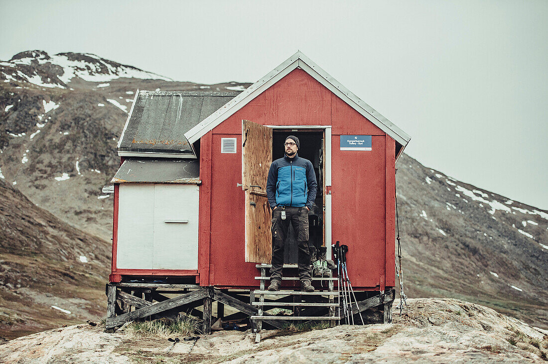 Hiker in front of a red cabin greenland, greenland, arctic.