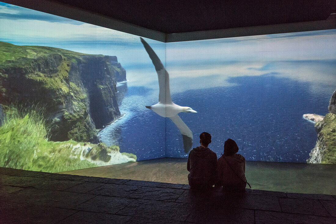 tow visitors watch animated introduction to the Cliffs of Moher at visitor centre, County Clare, Ireland, Europe