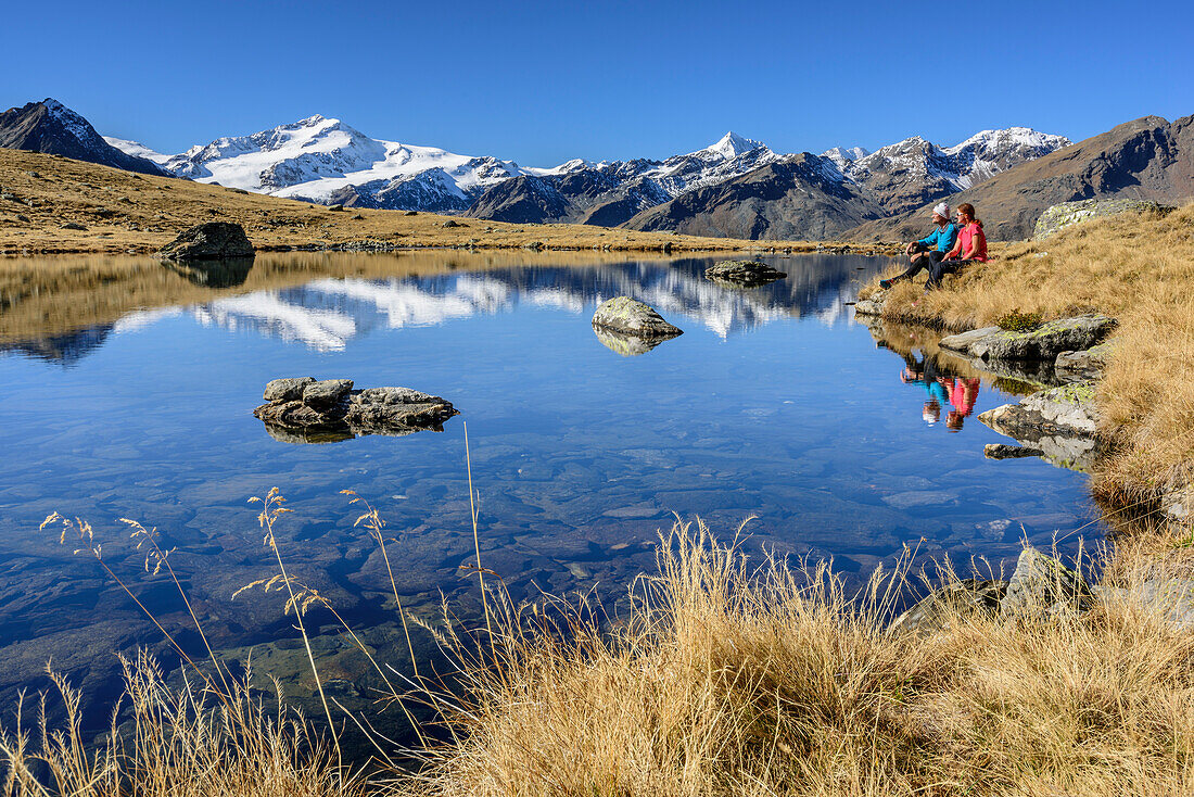 Man and woman sitting at mountain lake with Cevedale in background, valley of Martelltal, Ortler group, South Tyrol, Italy