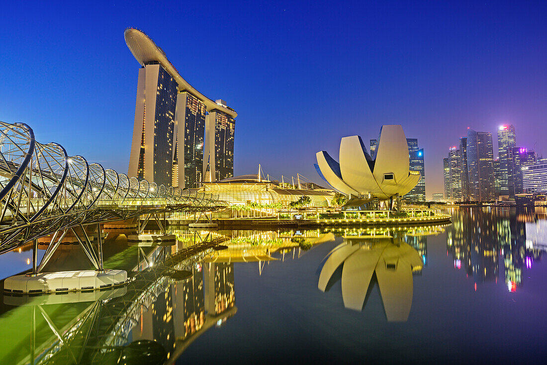 Illuminated skyline of Singapore with Helixbridge, Marina Bay Sands and ArtScience Museum reflecting in Marina Bay, Singapore