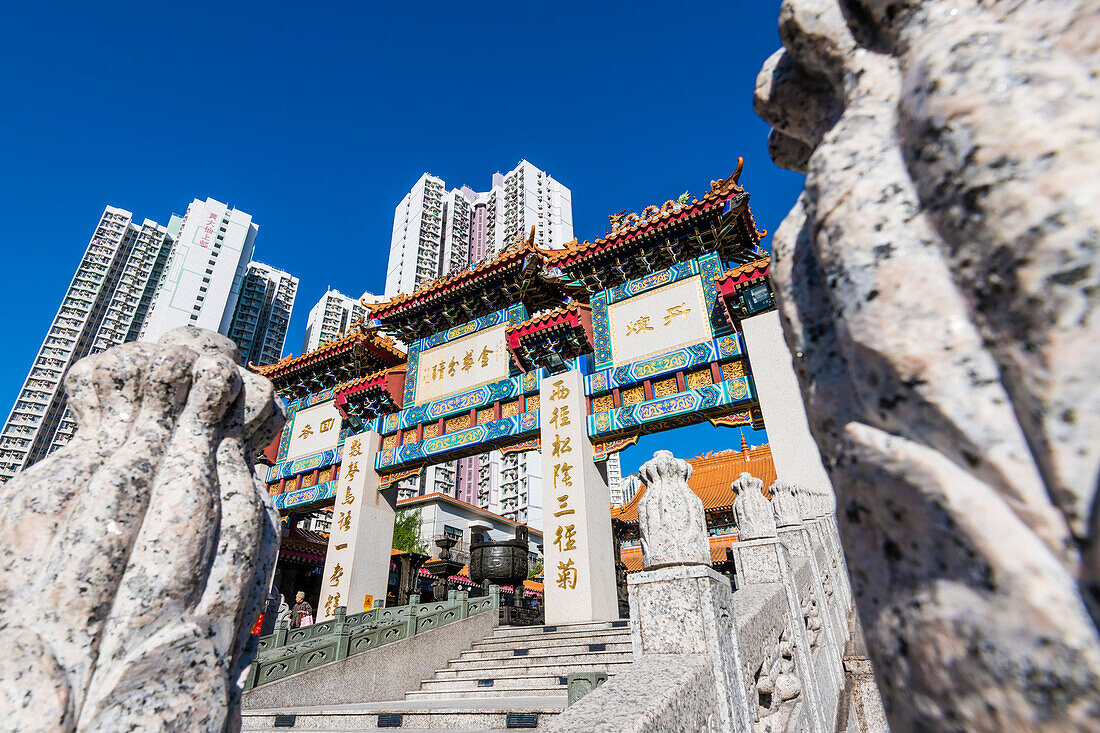 Das Eingangsportal zum taoistischen Wong Tai Sin Tempel umrahmt von den Wohnhochhäusern in Kowloon, Hongkong, China, Asien