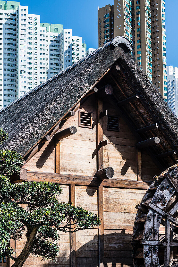 The water mill in the Nan Lian Garden in front of the scenery of the skyscrapers in Kowloon, Hong Kong, China, Asia