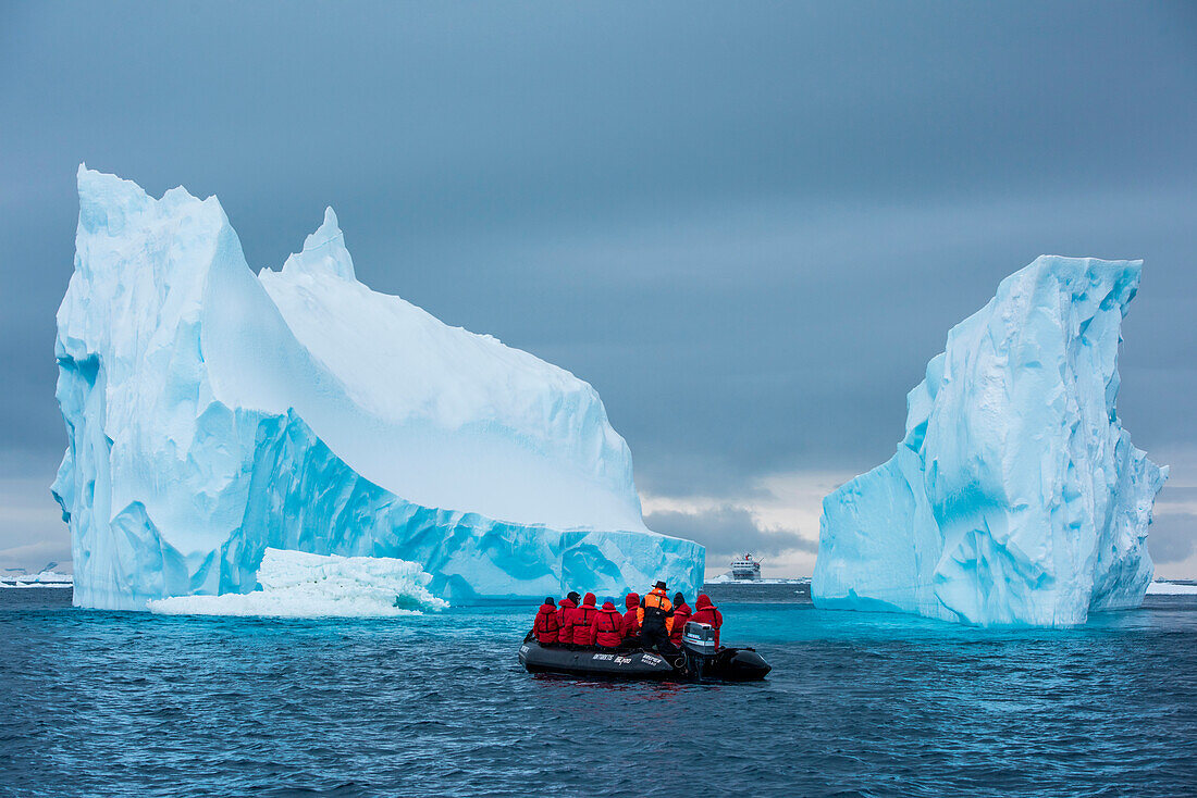 Ein Zodiac Schlauchboot und das Expeditions- Kreuzfahrtschiff MS Bremen (Hapag-Lloyd Cruises) werden von einem turmhohen Eisberg überragt, Active Sound, Antarktis