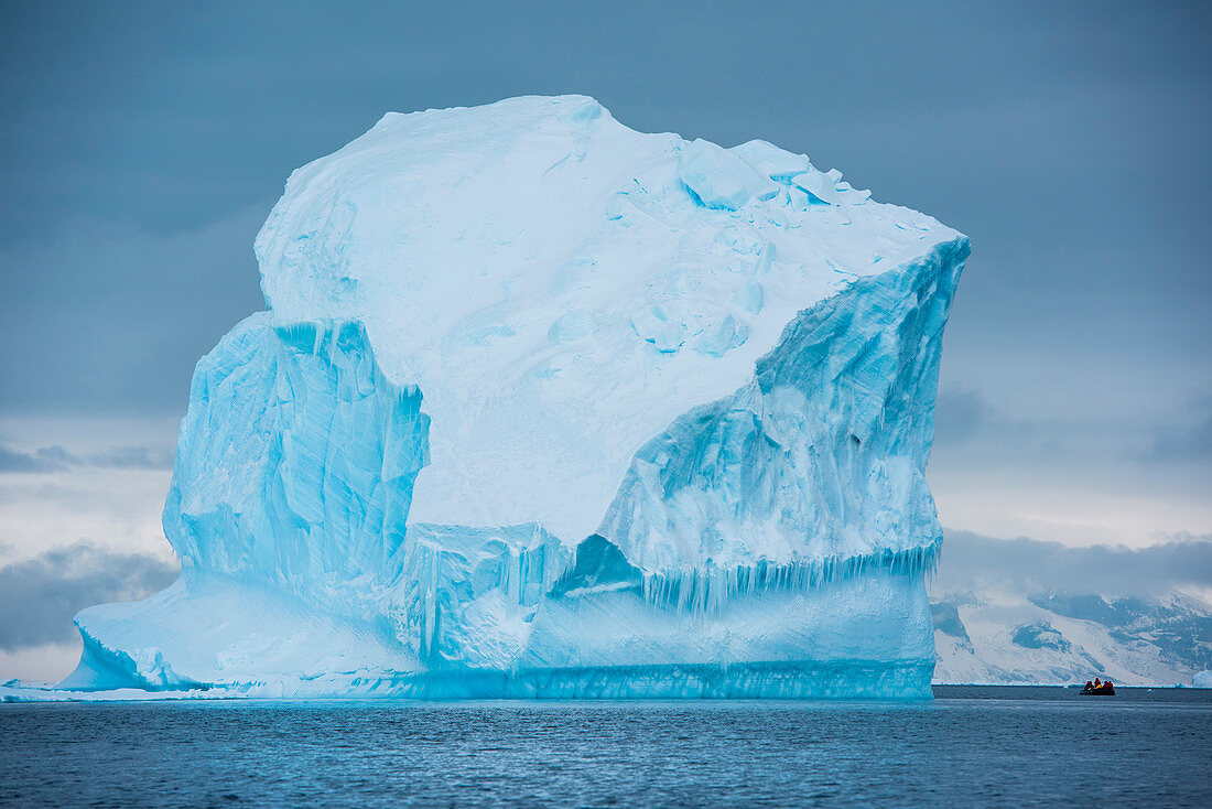 Ein Zodiac Schlauchboot von Expeditions-Kreuzfahrtschiff MS Bremen (Hapag-Lloyd Kreuzfahrten) wird von einem turmhohen Eisberg überragt, Active Sound, Antarktis