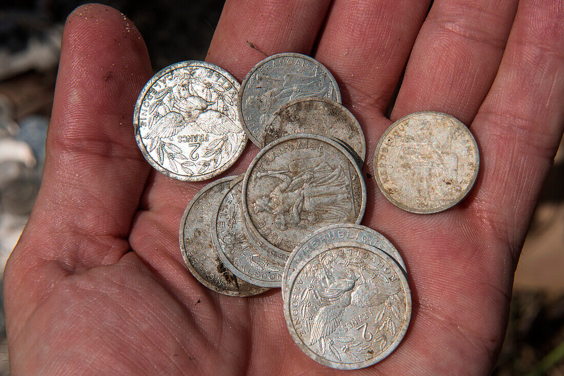 Hand holds New Caledonian coins left at the base of a cross atop a hill, Ile des Pins, New Caledonia, South Pacific