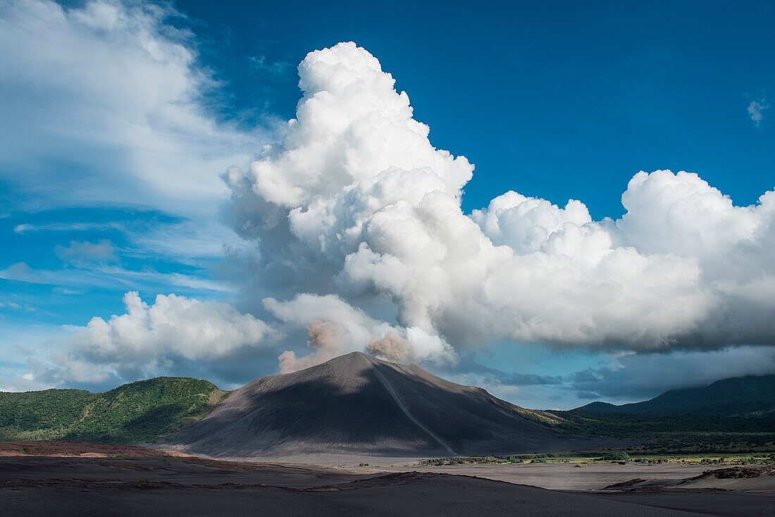 View from a distance to Mount Yasur volcano decked by brown and white clouds and surrounded by blue skies, Tanna Island, Vanuatu, South Pacific