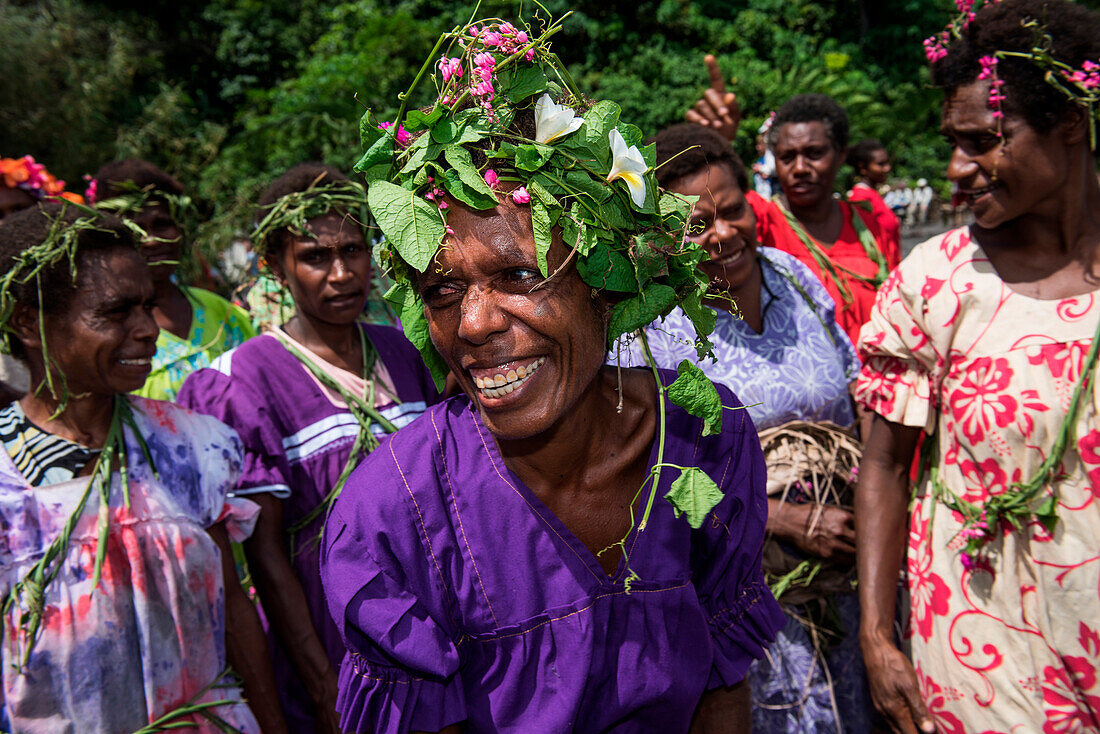Eine einheimische Frau in einem lilafarbenen Kleid und Kopfbedeckung aus Blättern und Blumen lacht inmitten einer Gruppe von Frauen, Wasisi Bay, Tanna Island, Vanuatu, Südpazifik