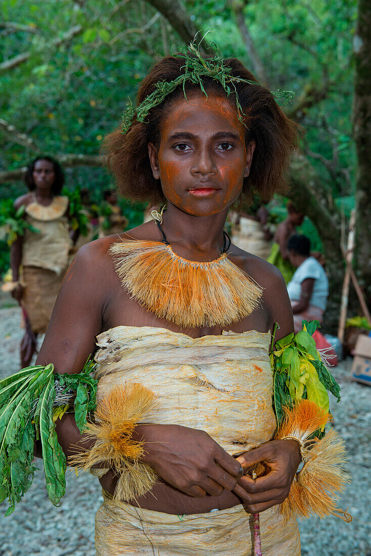 Eine junge Frau in traditioneller Kleidung aus Pflanzenmaterial und grünem Kopfschmuck steht auf einer Lichtung und bereitet sich auf eine Tanzvorführung vor, Nendo Island, Santa Cruz-Inseln, Salomonen, Südpazifik
