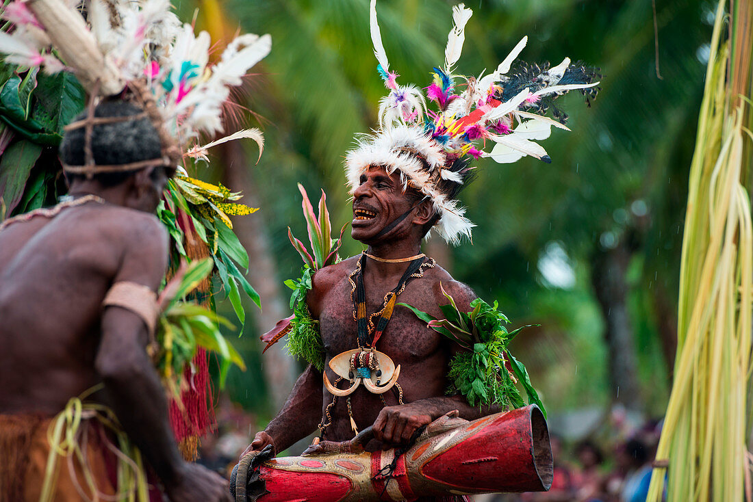 Ein Mann in traditioneller Tracht und Kopfschmuck lächelt während er eine Trommel hält, Kopar, East Sepik, Papua-Neuguinea, Südpazifik