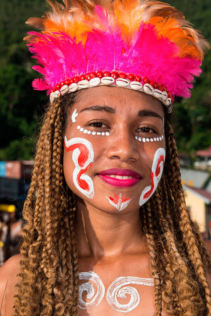 A woman with face-painting, a headdress of feathers and shells and braided hair smiles into the camera prior to a cultural performance, Port Numbay, Jayapura, Papua, Indonesia, Asia
