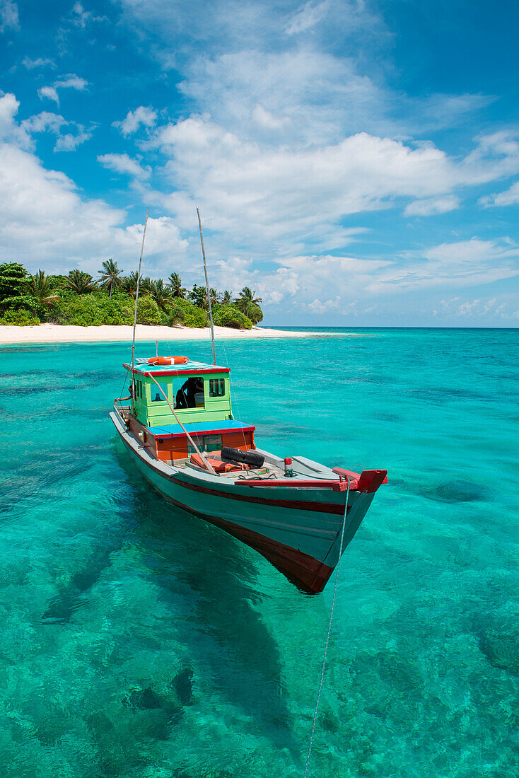 A colorful boat drifts in clear turquoise water off an island, Senua Island, Riau Archipelago, Indonesia, Asia