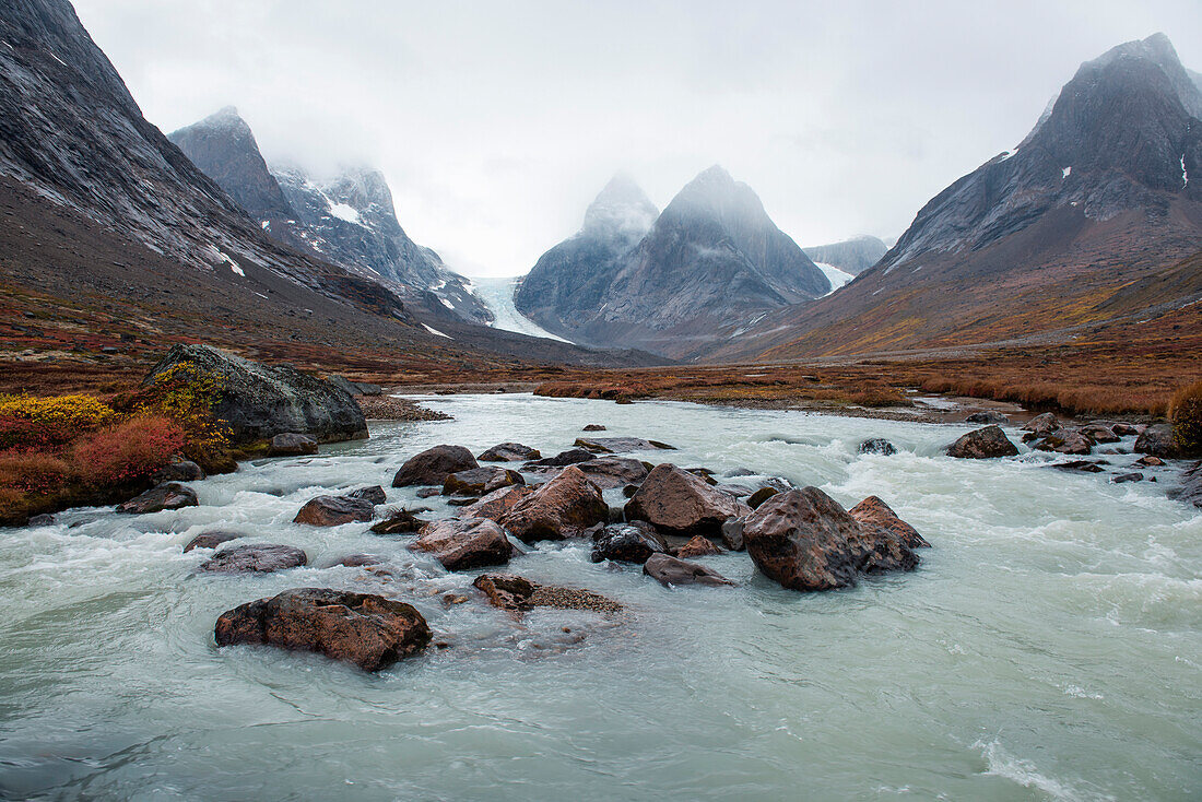 A glacial stream of milky-green water rushes over rocks in a mountainous, autumnal tundra landscape, Dronning Marie Dal (Valley), Skjoldungen Fjord, Southeast Greenland