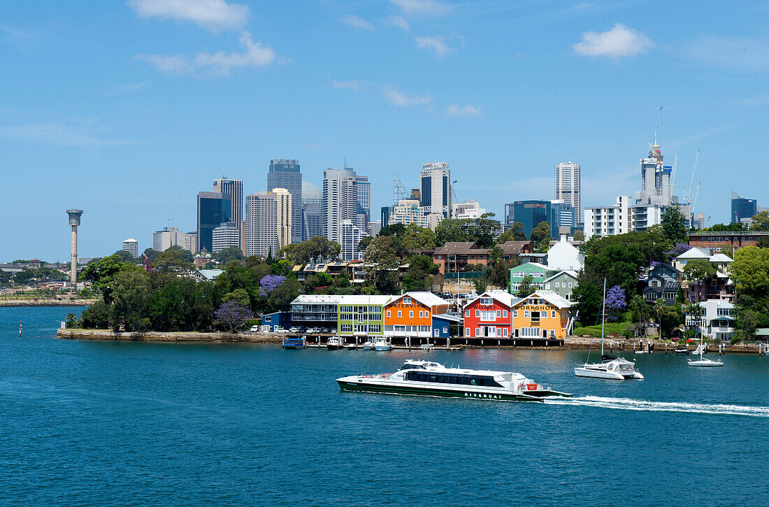 Farbenfrohe Bootshäuser in der Mort Bay, mit der City von Sydney im Hintergrund, Sydney, New South Wales, Australien