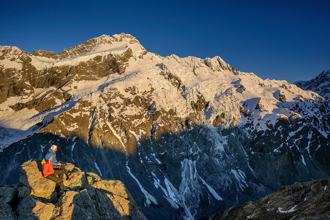 Man and woman sitting on rock and looking towards Mount Sefton and Footstool, from Mueller Hut, Hooker Valley, Mount Cook National Park, UNESCO Welterbe Te Wahipounamu, Lake Pukaki, Canterbury, South island, New Zealand