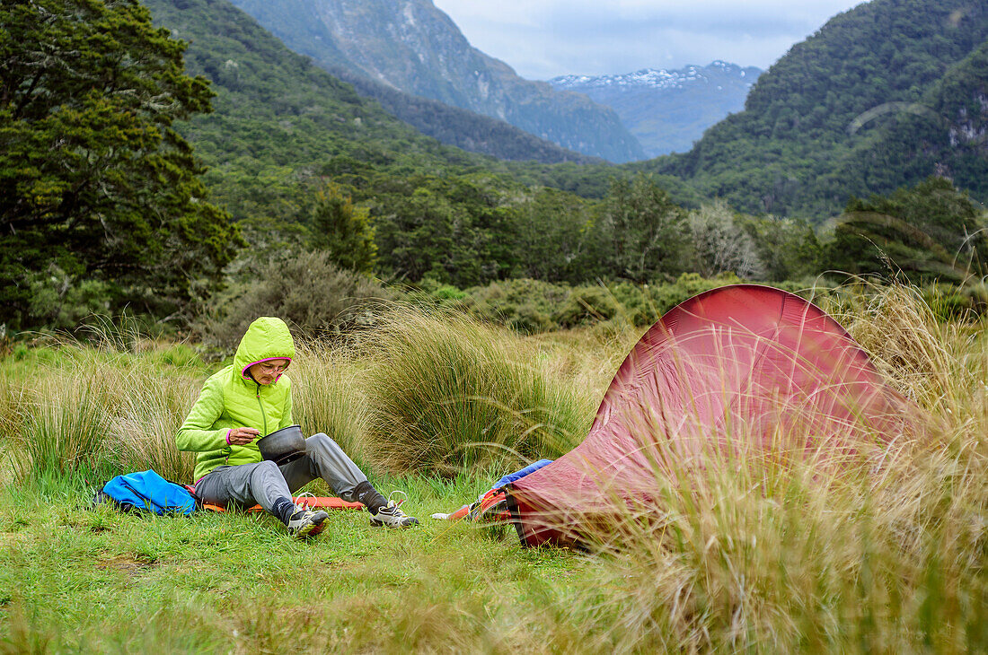 Woman sitting near tent and eating, Iris Burn Hut, Kepler Track, Great Walks, Fiordland National Park, UNESCO Welterbe Te Wahipounamu, Southland, South island, New Zealand