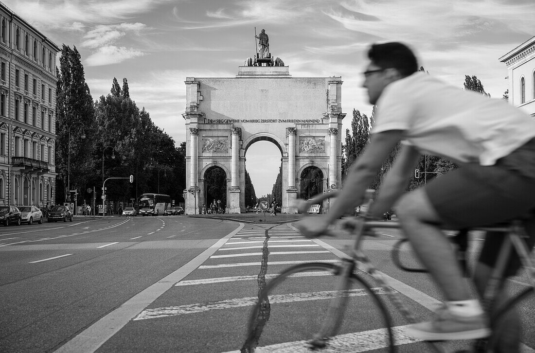 Street scene in front of Siegestor, a cyclist crossing the street, Munich, Upper Bavaria, Germany