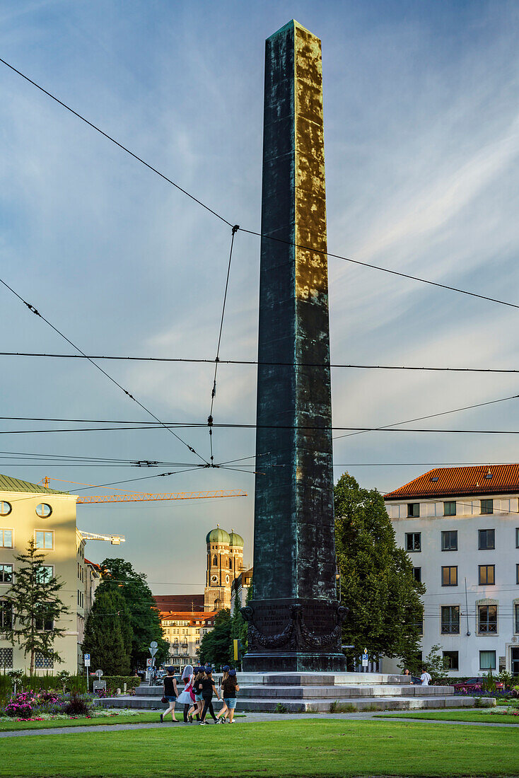 Eine Gruppe kostümierter Mädchen quert den Obelisk am Karolinenplatz, im Hintergrund die Frauenkirche, München, Oberbayern, Deutschland