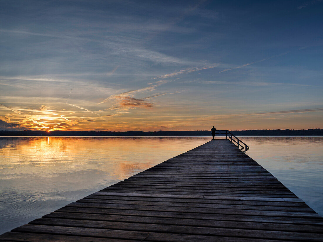 A woman standing on a jetty at sunset on the eastern shore of lake Starnberg, Ambach, Upper Bavaria, Germany