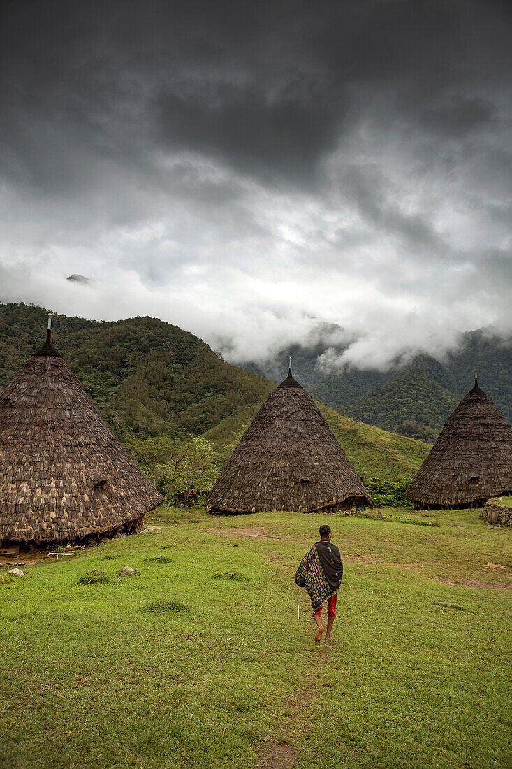 INDONESIA, Flores, a man walks towards his traditional thatched home in Wae Rebo Village, the home is treaditionally referred to as Mbaru Niang