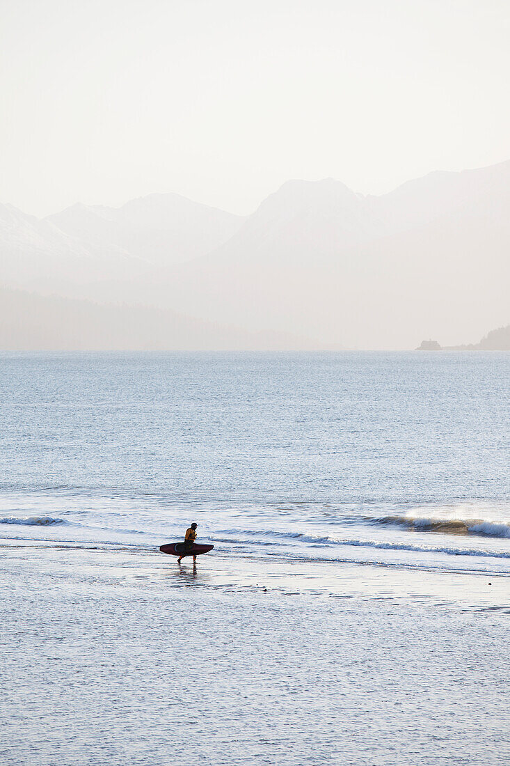 Surfer Walking On Beach, Kachemak Bay With Kenai Mountains In The Background, Homer Spit, Southcentral Alaska, USA