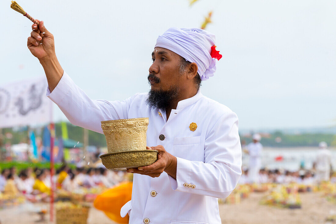 A Religious Man Sprinkles Water On Local Balinese People At A Ceremony At The Beach; Bali