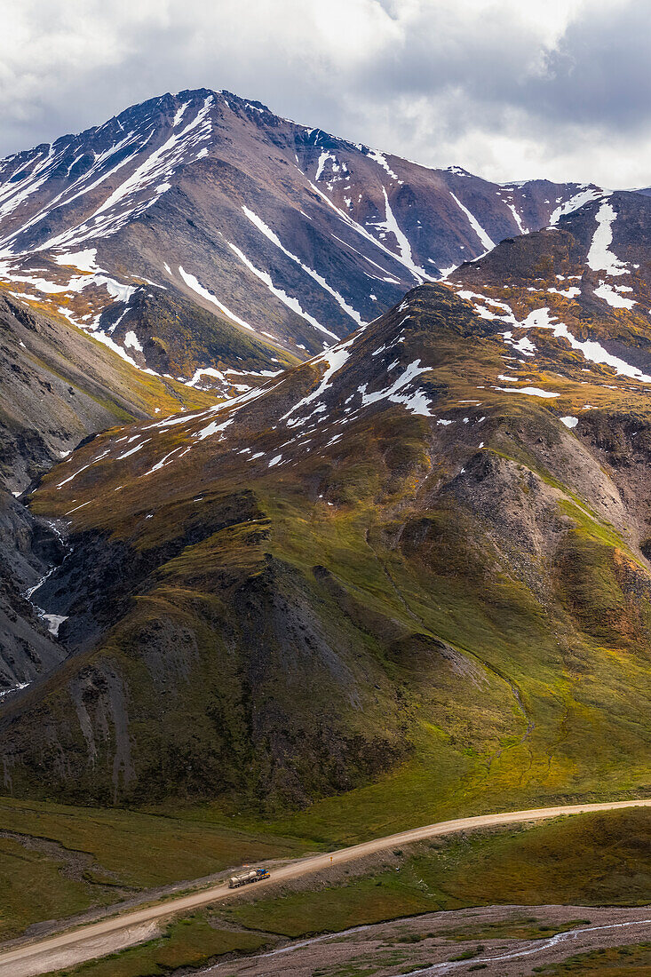 A truck approaches Atigun Pass along the Dalton Highway with the mountains of the Brooks Range towering overhead; Alaska, United States of America