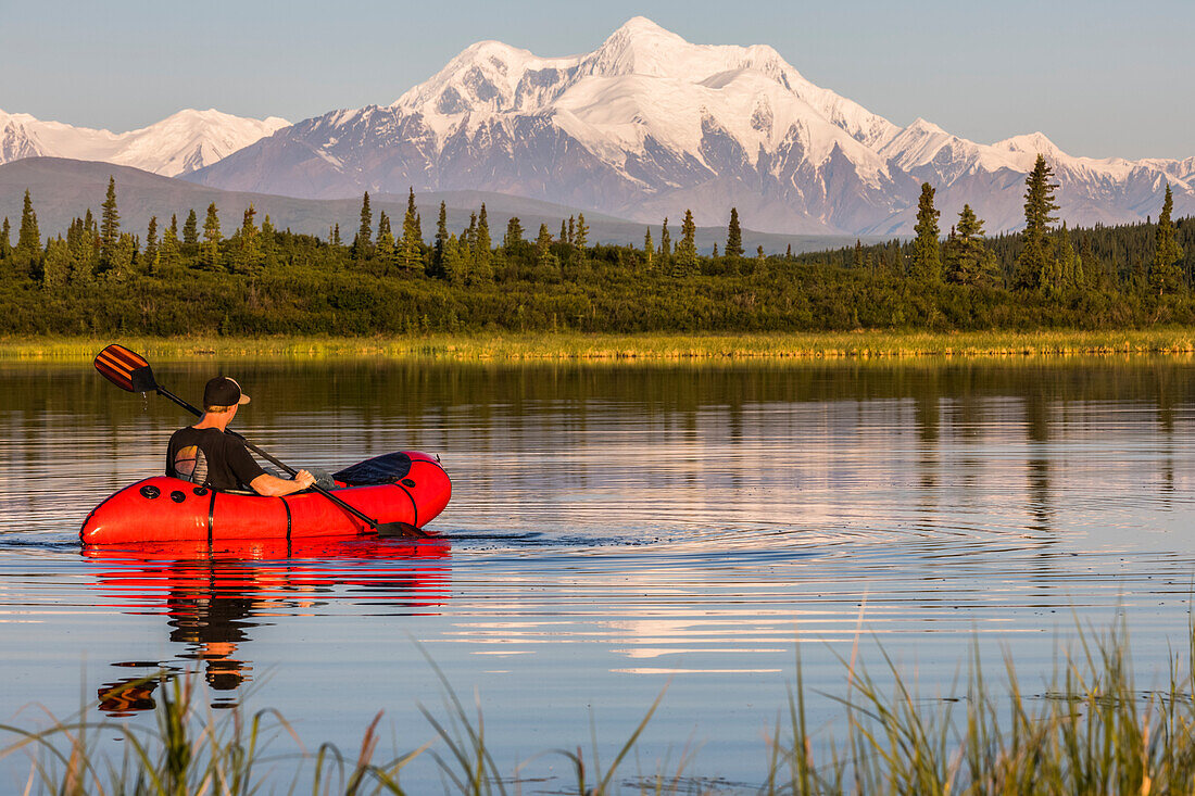 A man paddles a pack raft across Donnelly Lake with Mt. Hayes towering in the distance; Alaska, United States of America