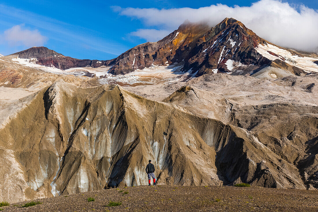 A man is dwarfed by the jagged, ash-covered Knife Creek Glaciers and Trident Volcano in the Valley of Ten Thousand Smokes in Katmai National Park; Alaska, United States of America