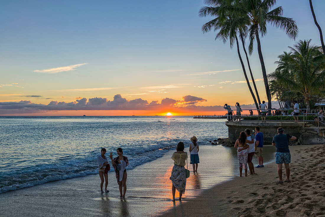 Tourists watch and photograph sunset on Waikiki Beach; Honolulu, Oahu, Hawaii, United States of America