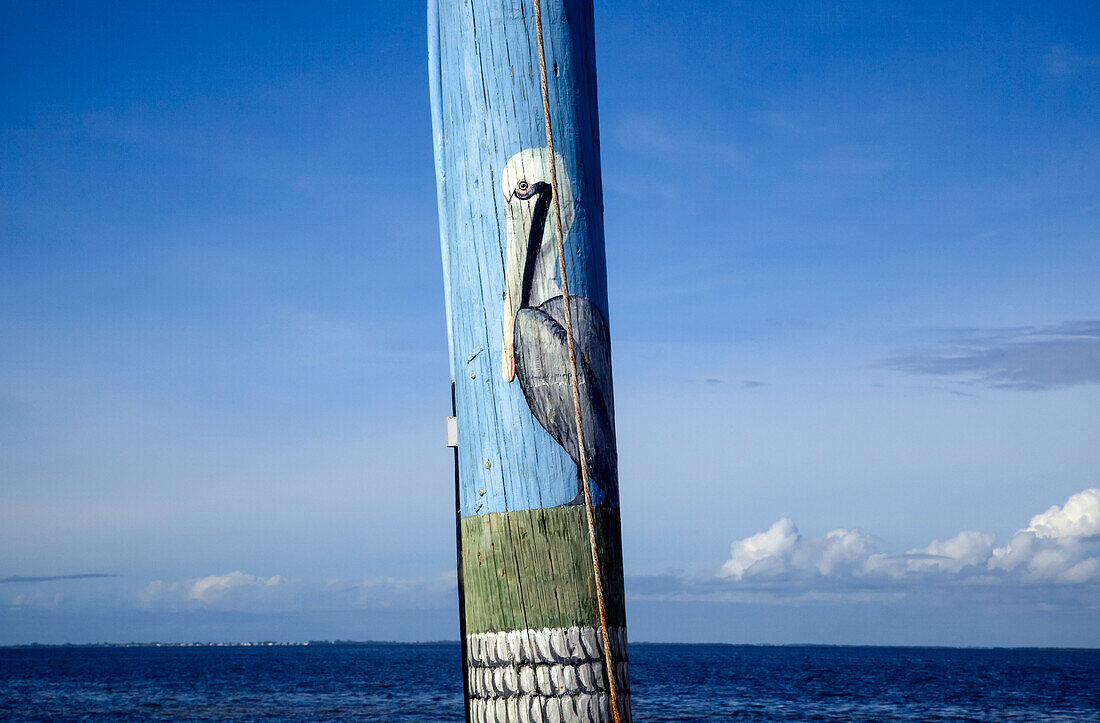 Close-up view of a pelican painted on a telephone pole with ocean and blue sky beyond; Pine Island, Florida, United States of America