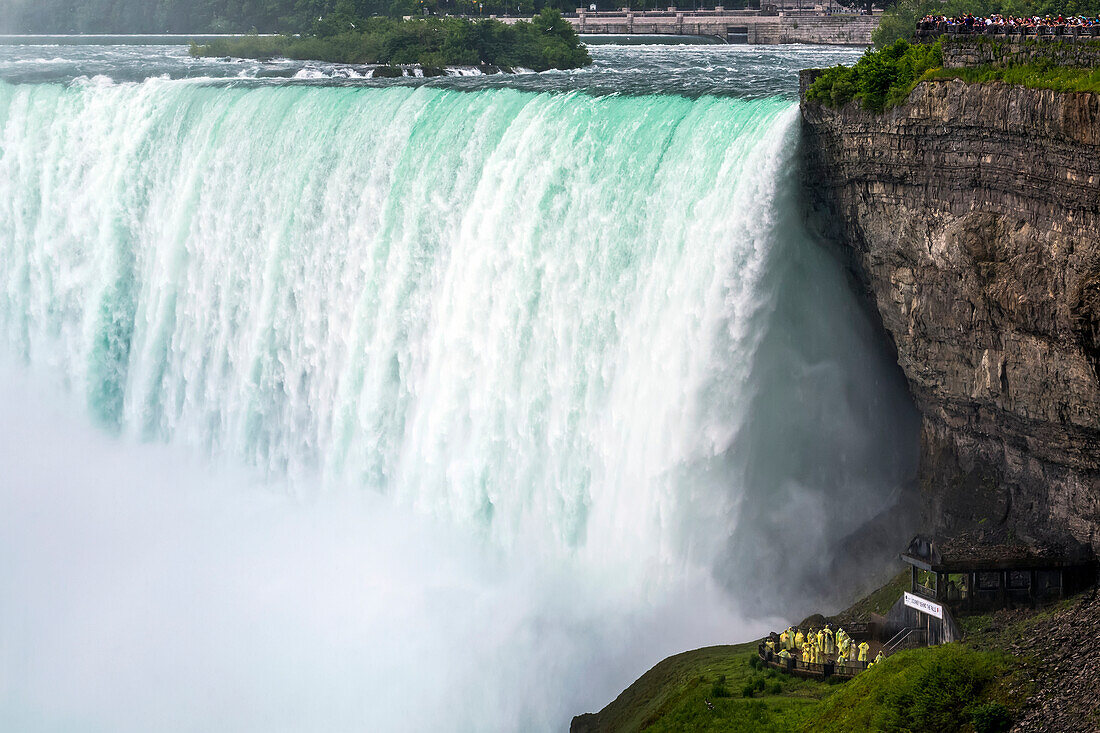 Close-up of Niagara Falls with cliffs and tourists standing on the viewing platforms; Niagara Falls, Ontario, Canada