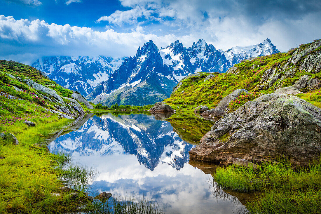 Aiguille des Charmoz, part of Aiguilles de Chamonix, reflects on Lac Flegere surrounded with green meadow, Aiguilles Rouges; Chamonix-Mont-Blanc, Haute-Savoie, France