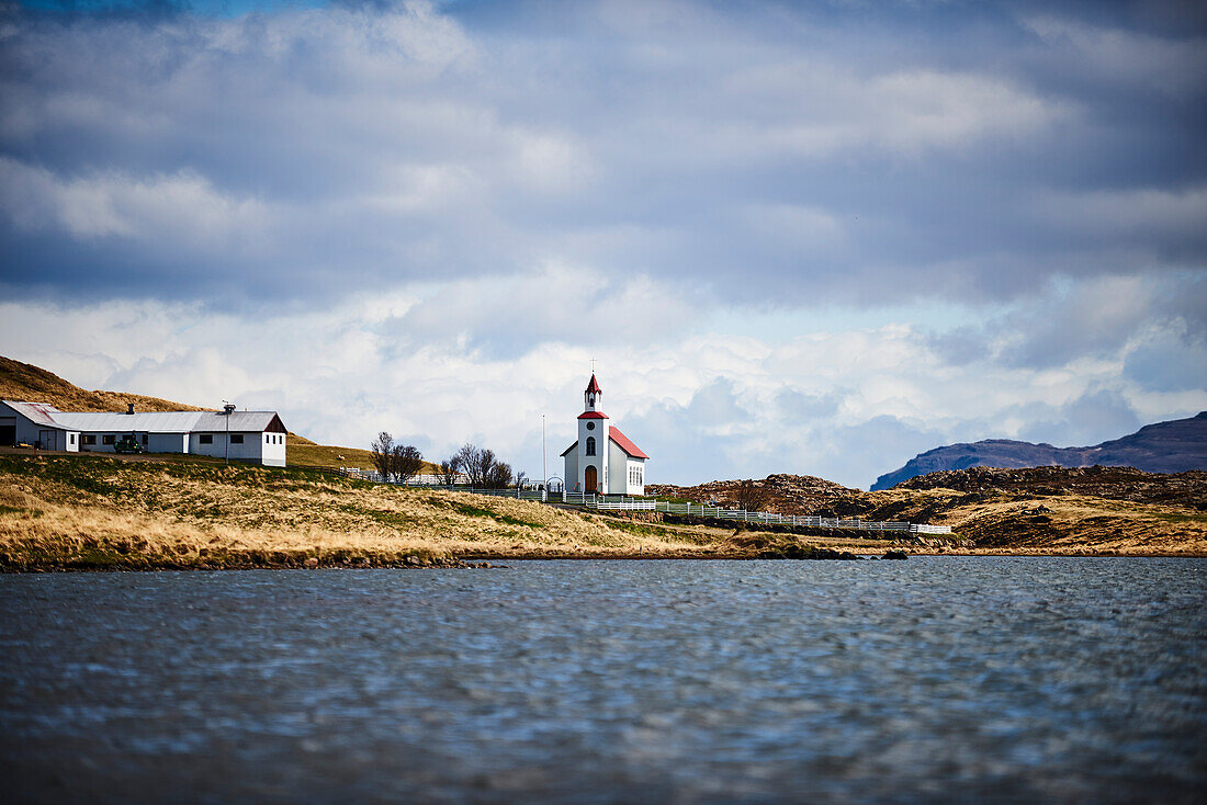 Church With A Red Roof, Barn And Farmhouse Along A Lake; Iceland